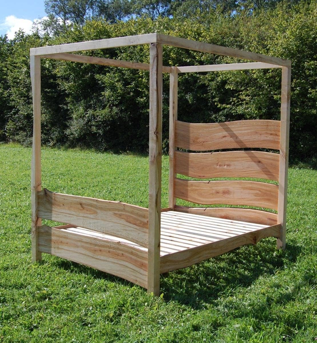 a wooden four poster handmade bed in a grassy area