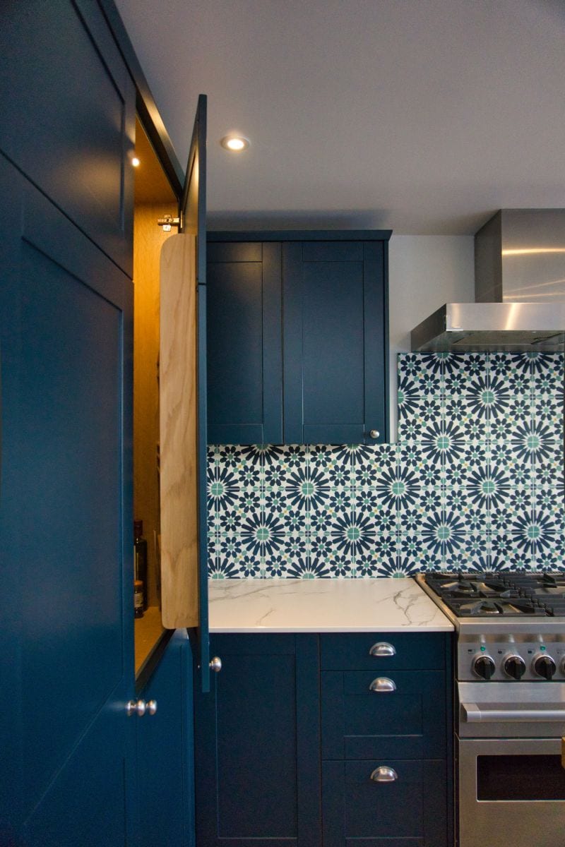 a kitchen with blue cabinets and a stove showing an open pantry door with lights inside