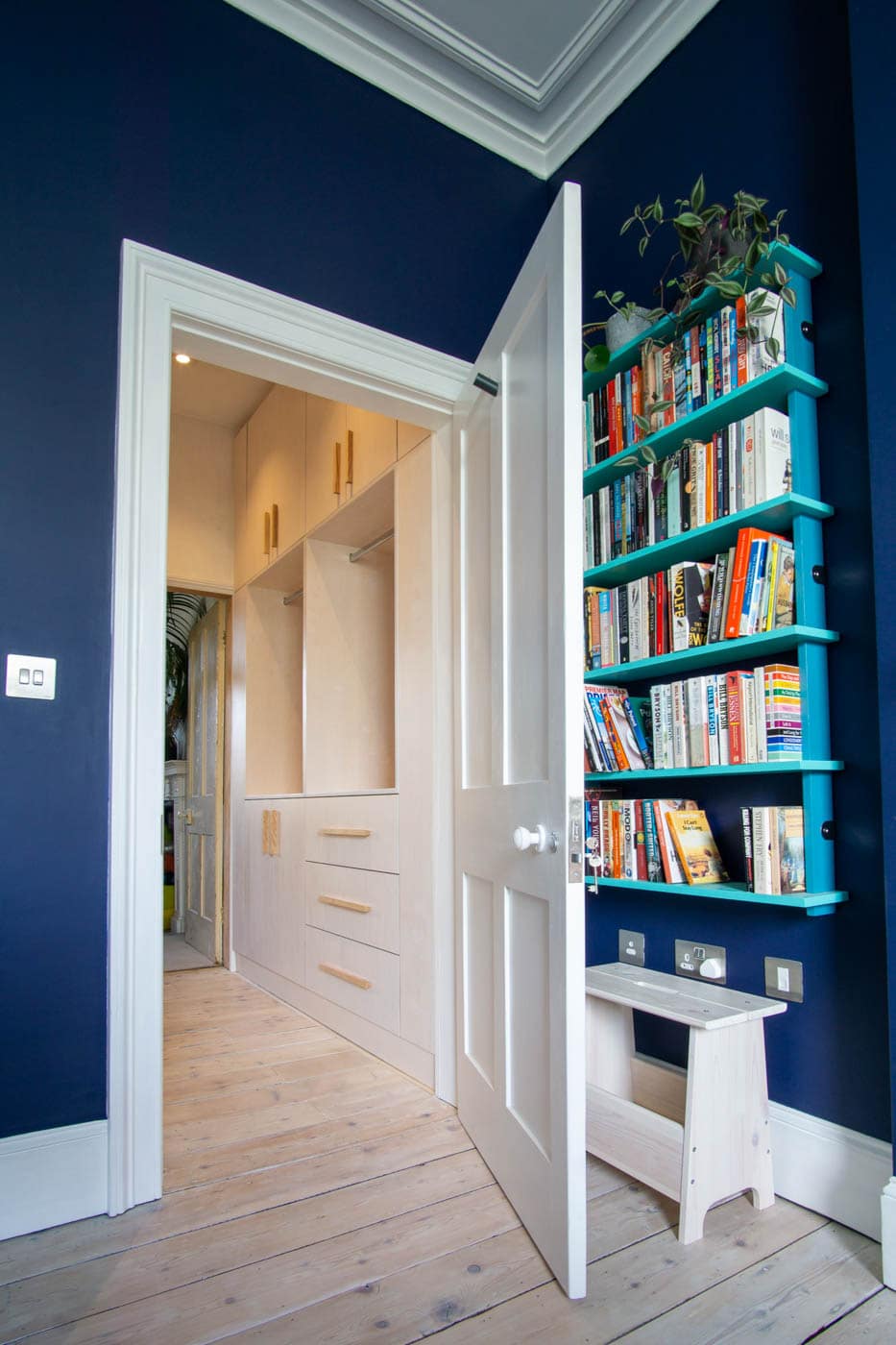 A blue walled room with a book shelf and a door.