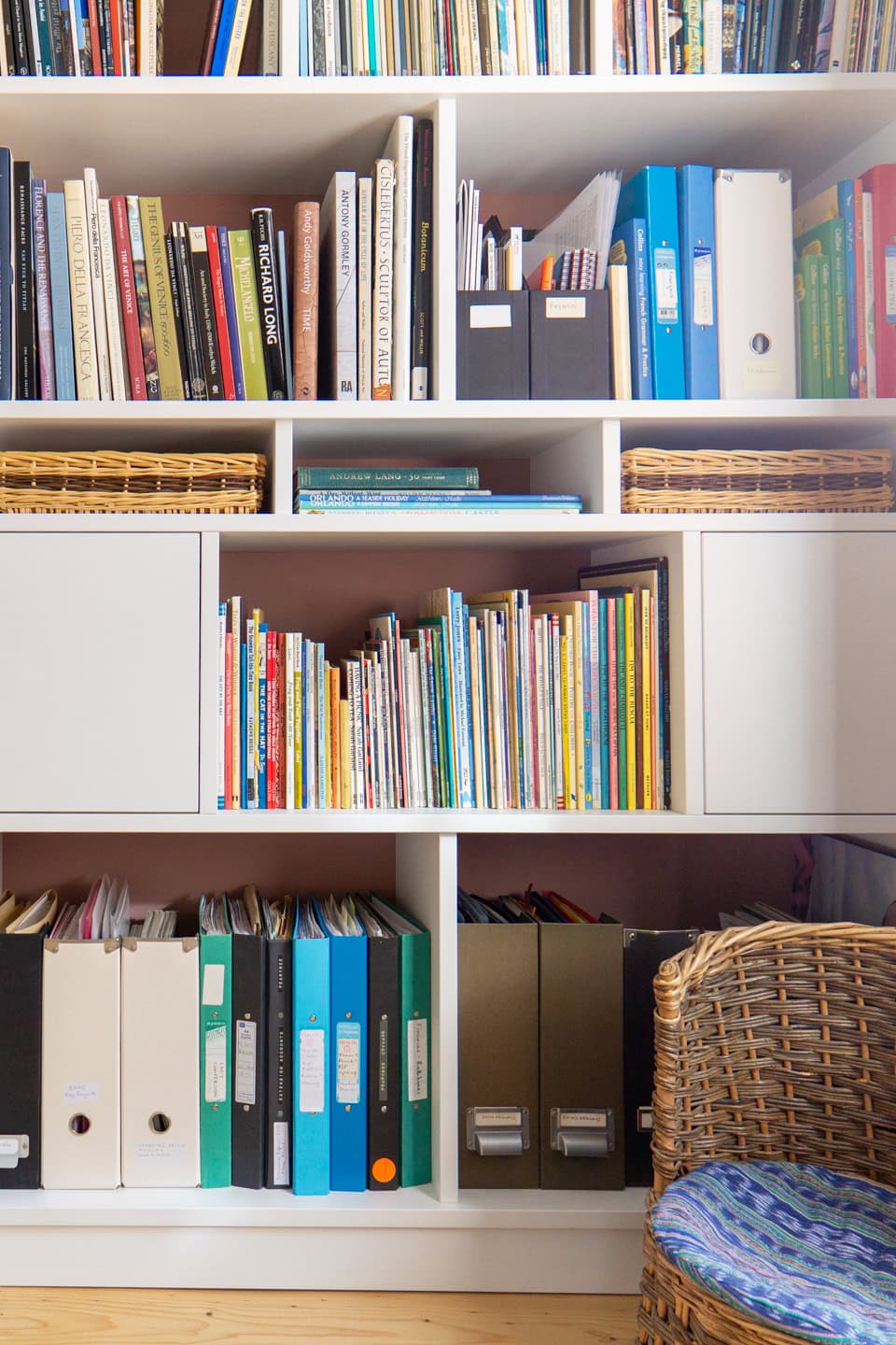 a shelf with books and binders small wicker peacock chair