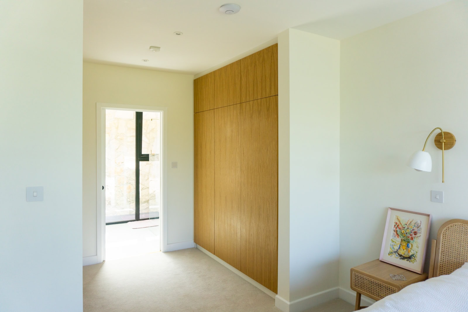 Bespoke handleless fitted wardrobes in Portishead, linking bedroom and en suite with flush oak-veneered doors