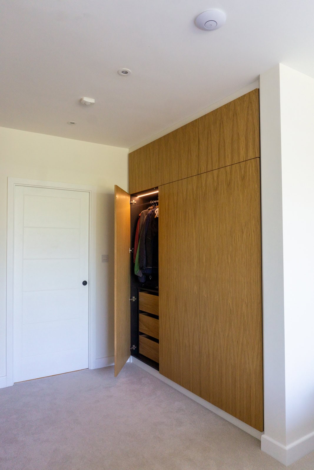 Oak handleless wardrobe with door open showing black interior and oak drawers and lighting