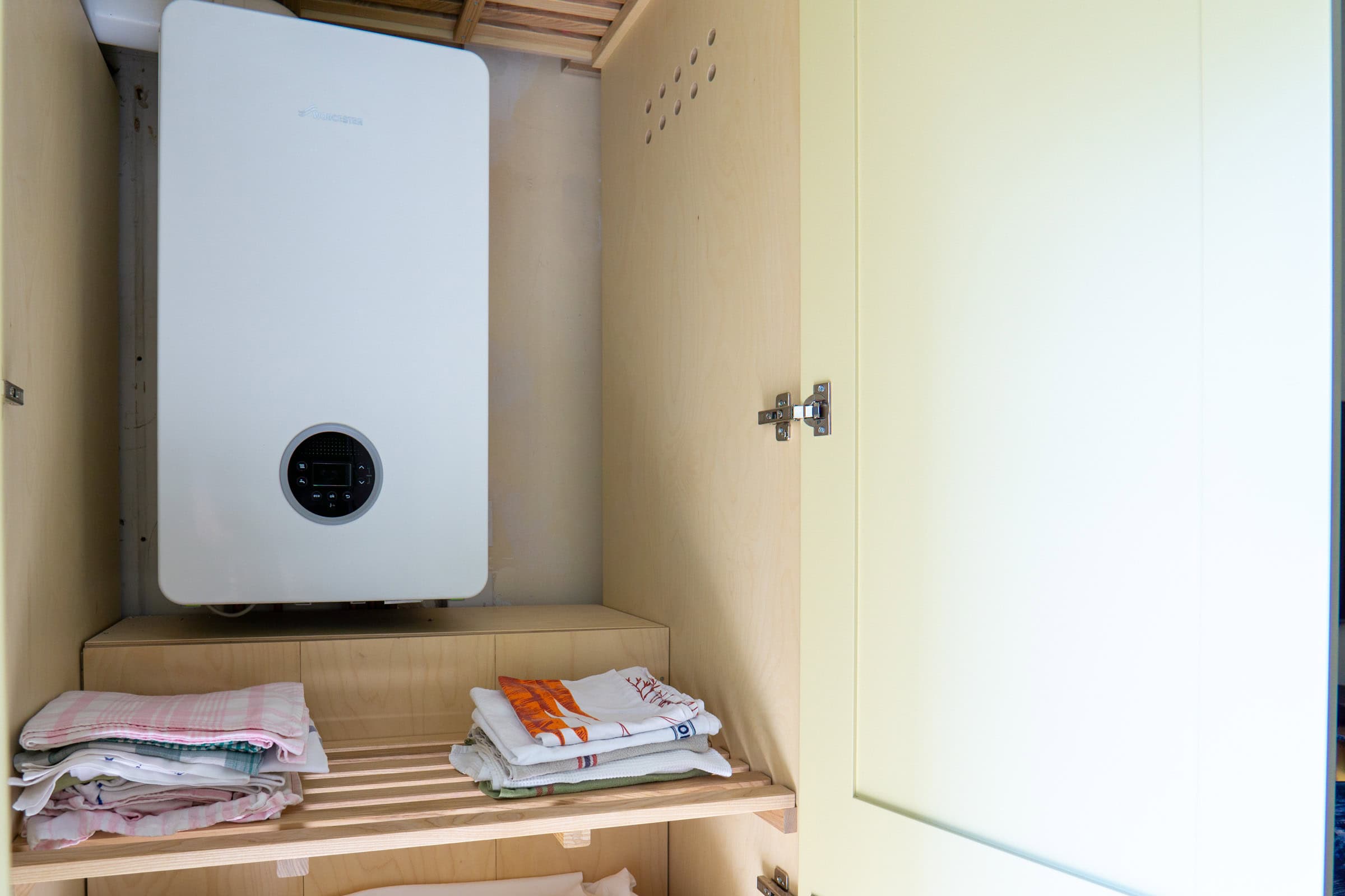 interior of a bespoke airing cupboard showing the boiler plywood interior and vent holes and slatted shelves